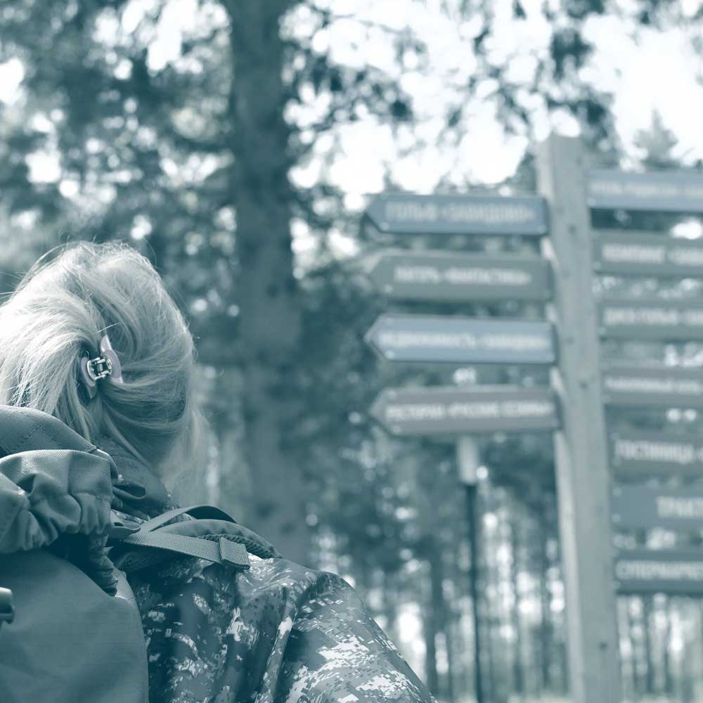 Photo of the back of a woman's head looking at signposts in a wooded trail. Showing how our employee benefits company helps you to build.