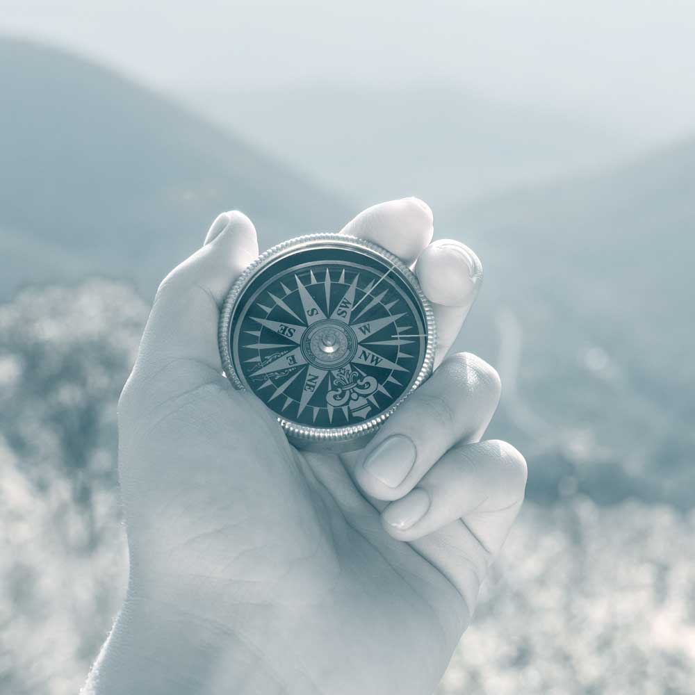 Photo of a hand holding a compass in the mountains, showing how a good employee benefits company can help you find the way.